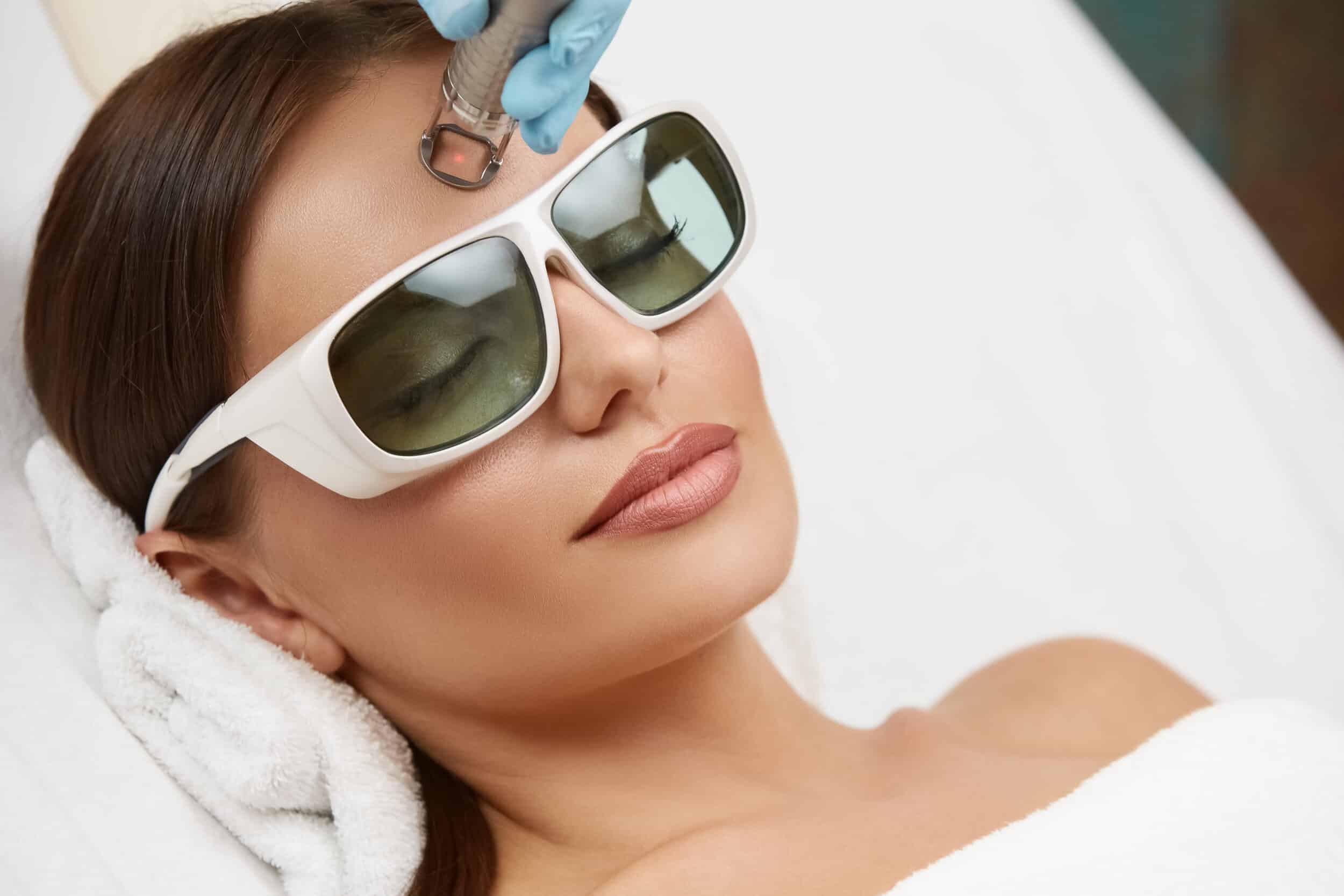 close up of beautiful woman doing laser procedure on her forehead wearing protection glasses